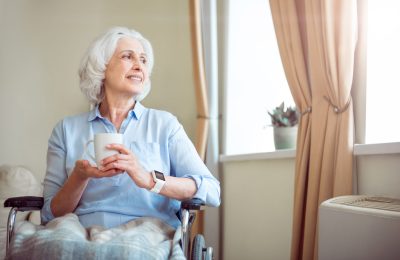 Tea time. Positive and delighted old woman in wheelchair with cup of tea